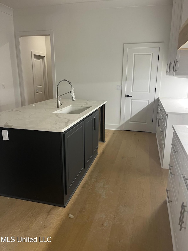 kitchen featuring white cabinetry, sink, light stone counters, an island with sink, and light hardwood / wood-style floors