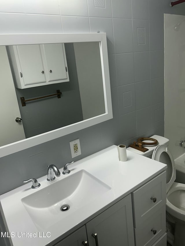 bathroom featuring toilet, vanity, tile walls, and tasteful backsplash