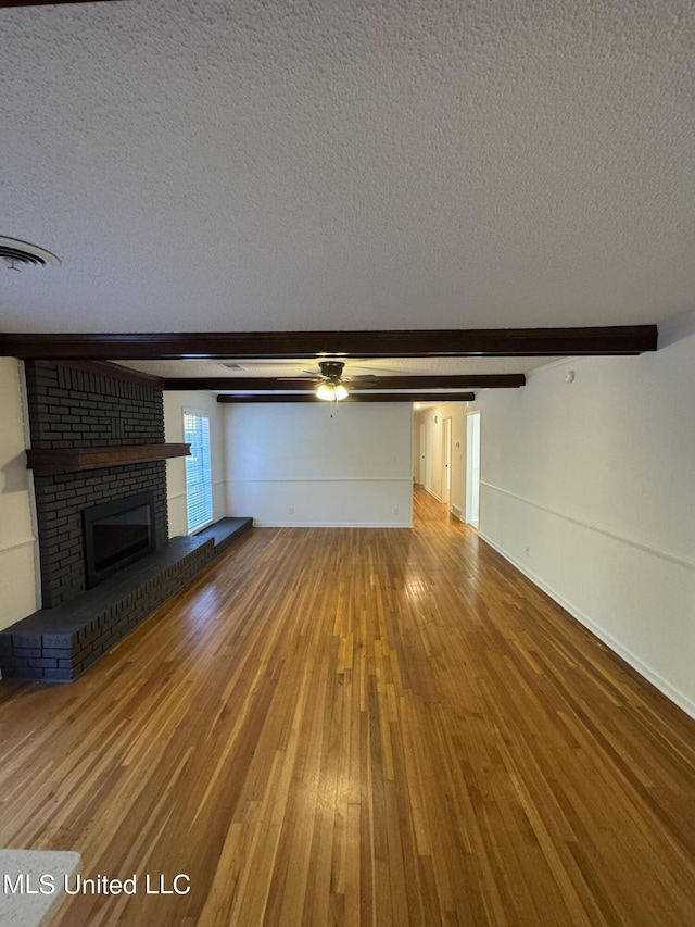 unfurnished living room featuring beamed ceiling, a textured ceiling, a fireplace, and hardwood / wood-style flooring