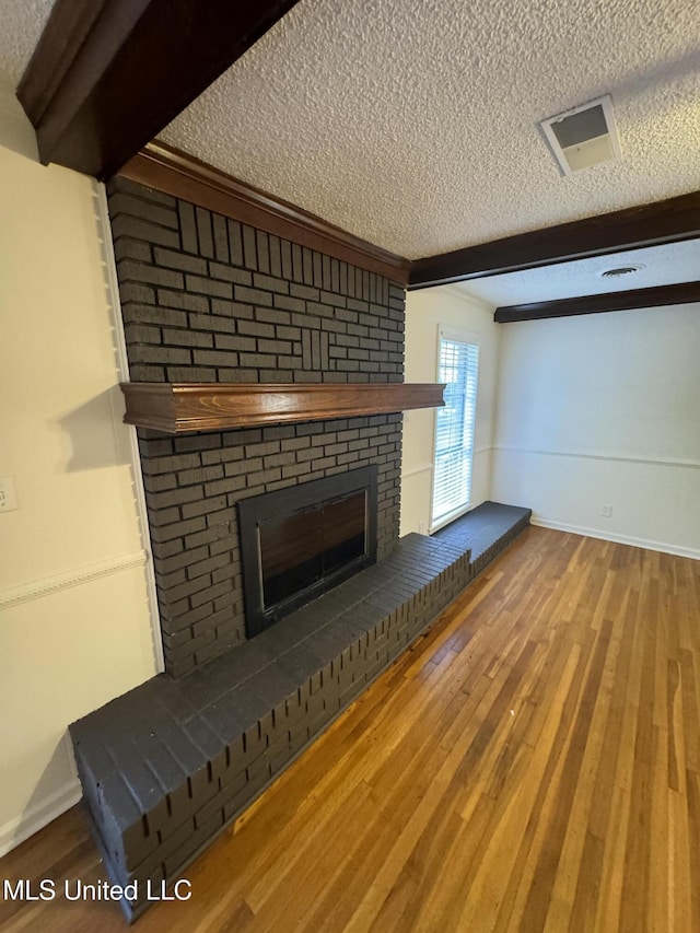 unfurnished living room with beam ceiling, hardwood / wood-style flooring, a textured ceiling, and a brick fireplace