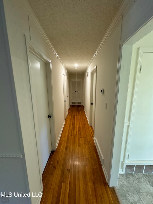 hall with ornamental molding, hardwood / wood-style floors, and a textured ceiling