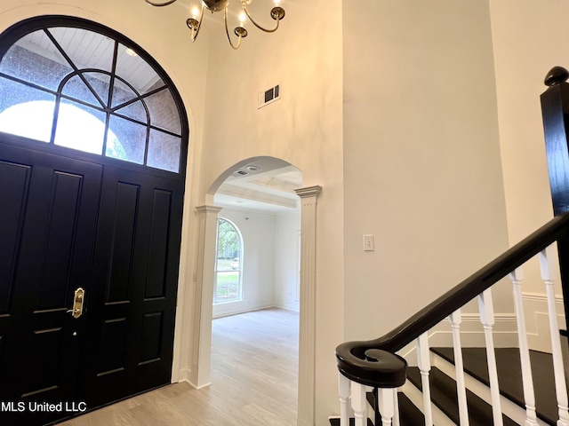 entrance foyer featuring arched walkways, wood finished floors, a chandelier, ornate columns, and baseboards