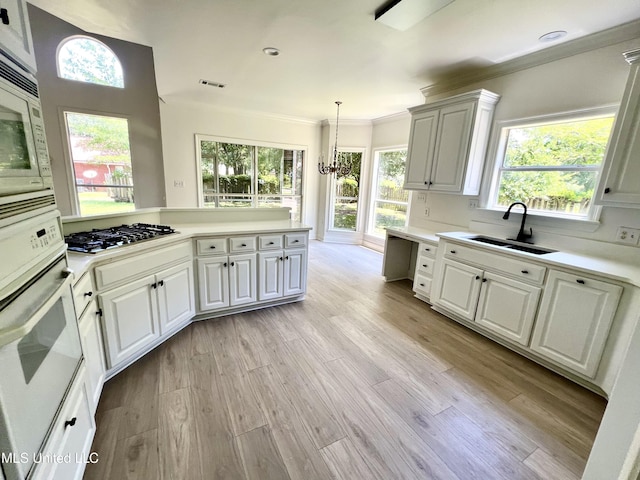 kitchen featuring white appliances, a sink, light countertops, light wood-style flooring, and ornamental molding