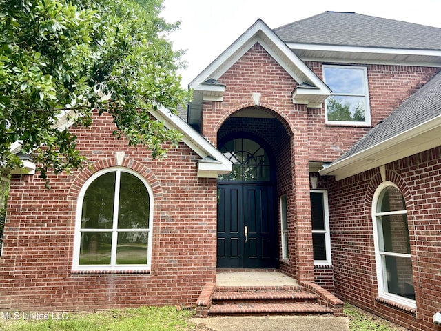 view of exterior entry with brick siding and roof with shingles
