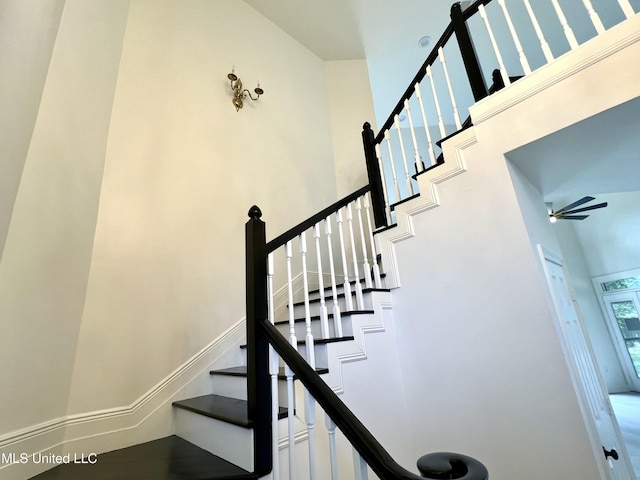 staircase with a towering ceiling and ceiling fan
