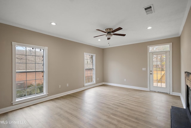 unfurnished living room with a fireplace, light wood finished floors, a wealth of natural light, visible vents, and ornamental molding