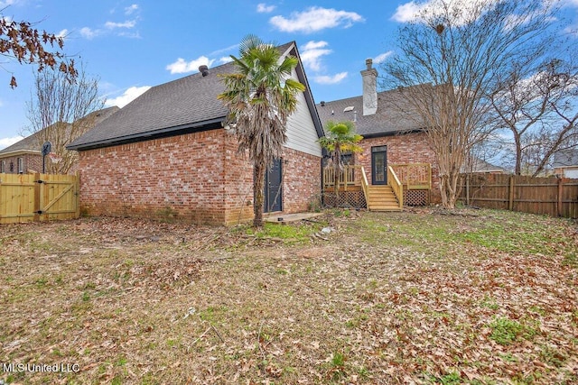 rear view of house featuring brick siding, a chimney, fence, and a gate