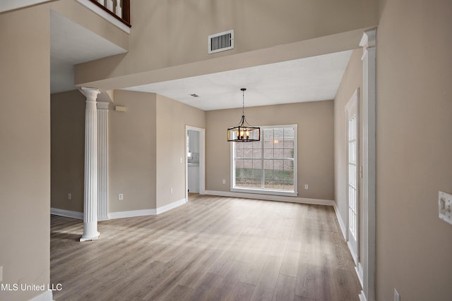 unfurnished dining area featuring baseboards, wood finished floors, visible vents, and ornate columns