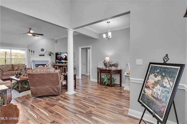 living area with a brick fireplace, baseboards, ceiling fan, light wood-type flooring, and decorative columns