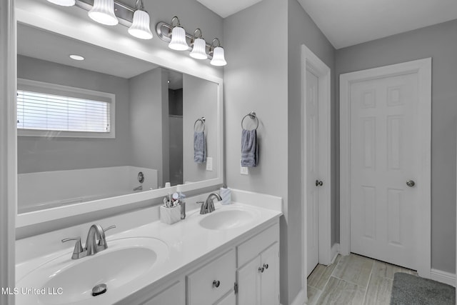 bathroom with double vanity, wood finish floors, a washtub, and a sink