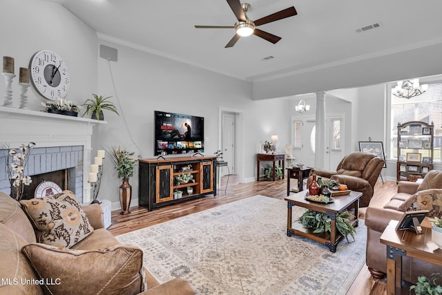 living room featuring visible vents, ornamental molding, a fireplace, wood finished floors, and ornate columns