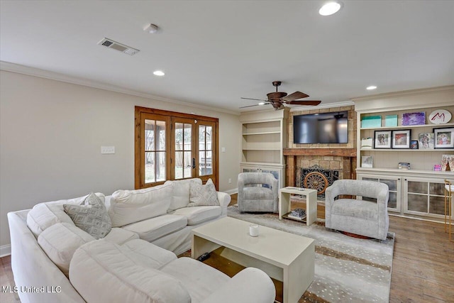 living room featuring hardwood / wood-style flooring, a stone fireplace, ornamental molding, and french doors