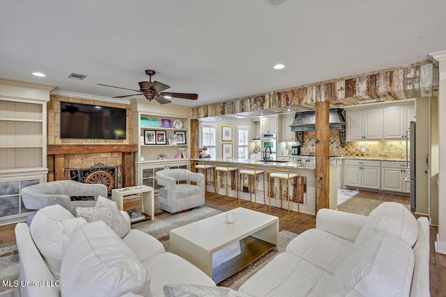 living room featuring sink, ornamental molding, ceiling fan, a fireplace, and light hardwood / wood-style floors