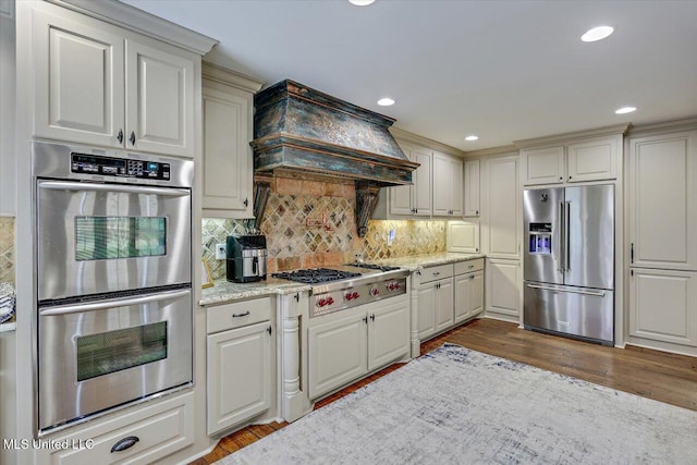 kitchen featuring dark hardwood / wood-style floors, tasteful backsplash, stainless steel appliances, light stone countertops, and custom range hood