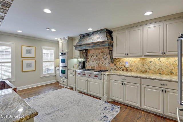 kitchen with decorative backsplash, appliances with stainless steel finishes, light stone countertops, and custom range hood