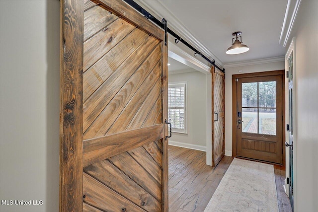 foyer entrance featuring light hardwood / wood-style flooring, ornamental molding, and a barn door