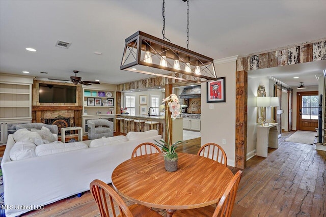 dining room with hardwood / wood-style floors, a fireplace, sink, ornamental molding, and ceiling fan