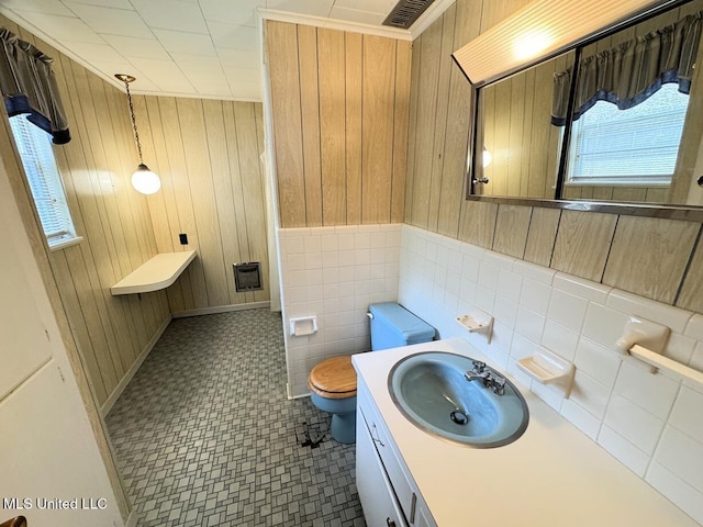 bathroom featuring tile walls, visible vents, toilet, wooden walls, and vanity