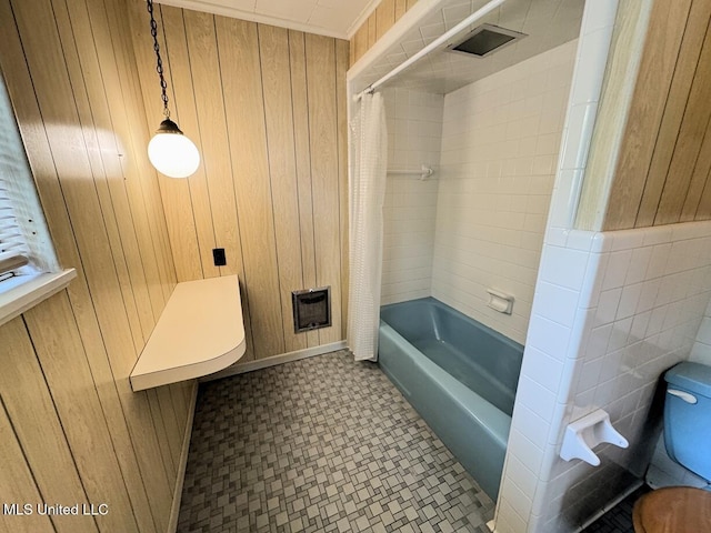 bathroom with tile walls, wooden walls, toilet, and shower / bath combo with shower curtain