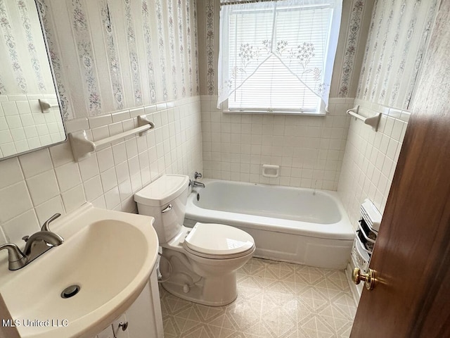 full bath with toilet, wallpapered walls, a bathing tub, and wainscoting