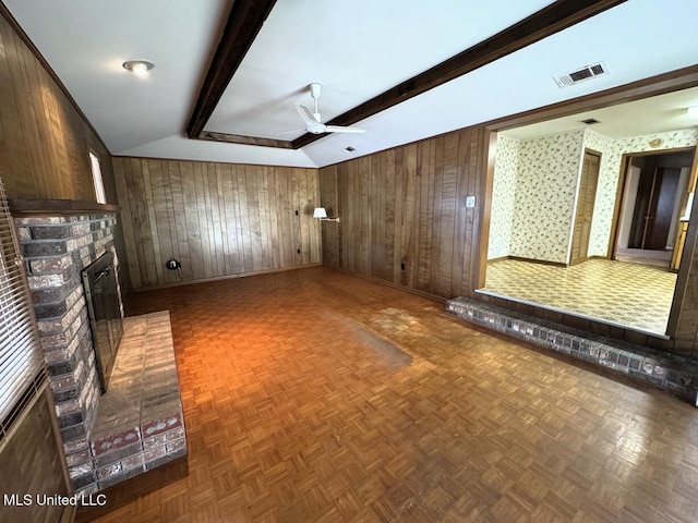 unfurnished living room with lofted ceiling with beams, wood walls, a fireplace, visible vents, and a ceiling fan