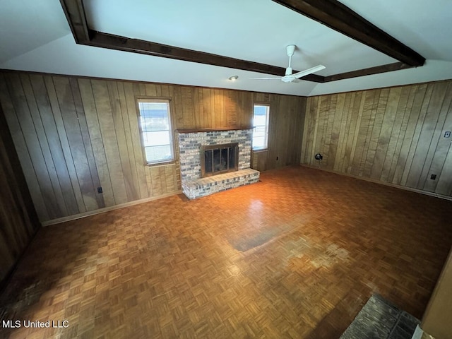 unfurnished living room with wooden walls, baseboards, ceiling fan, a fireplace, and beam ceiling