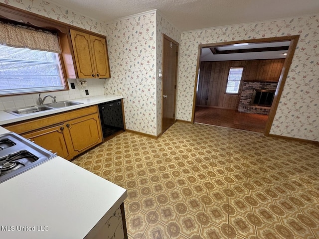 kitchen with black dishwasher, a fireplace, brown cabinetry, a sink, and wallpapered walls