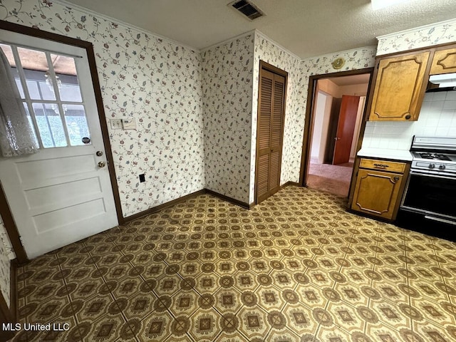 kitchen with visible vents, gas range, under cabinet range hood, baseboards, and wallpapered walls