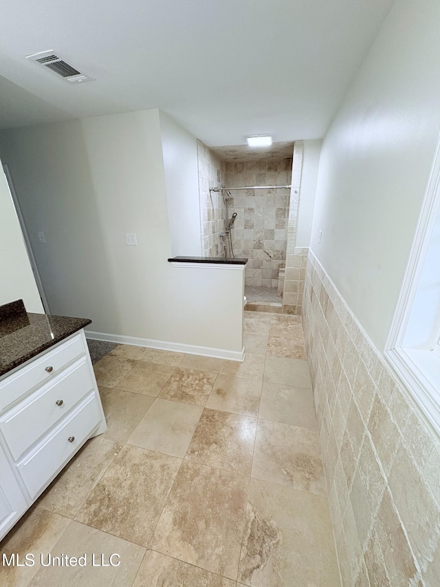 bathroom with visible vents, a tile shower, and vanity