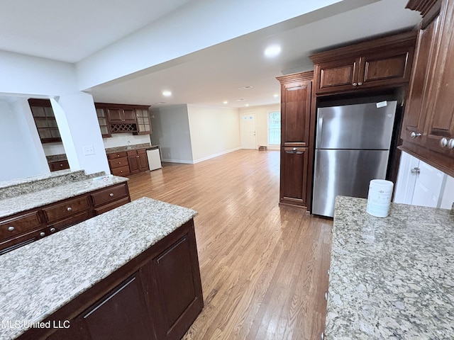 kitchen with white dishwasher, light stone countertops, light wood-style floors, freestanding refrigerator, and baseboards
