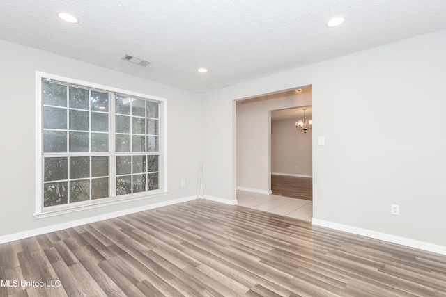 empty room featuring a notable chandelier, hardwood / wood-style floors, and a textured ceiling