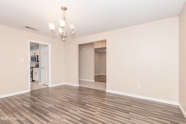 empty room featuring hardwood / wood-style flooring, a textured ceiling, and an inviting chandelier