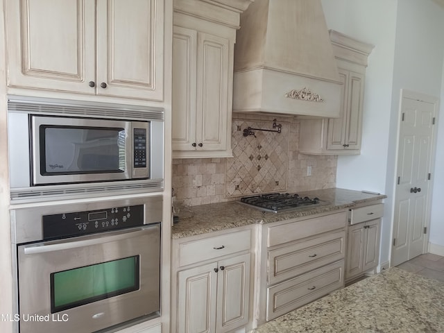 38 3rd St, Cleveland, MS 38732 - kitchen with light stone countertops, premium range hood, cream cabinetry, backsplash, and stainless steel appliances