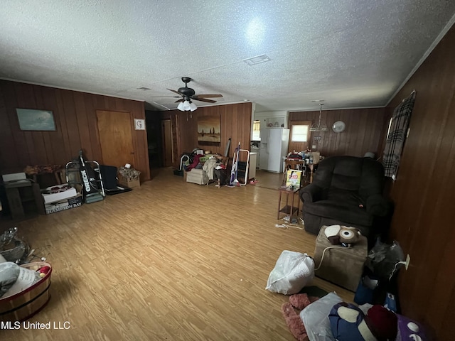 living room featuring ceiling fan, wooden walls, light hardwood / wood-style floors, and a textured ceiling