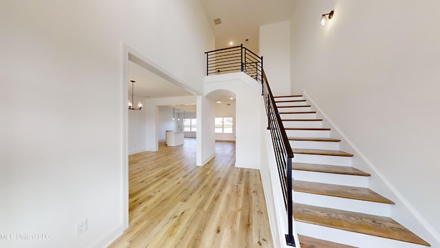 stairway featuring a chandelier, wood-type flooring, and a high ceiling