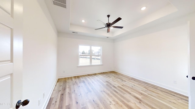 unfurnished room with light hardwood / wood-style flooring, ceiling fan, and a raised ceiling