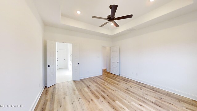 empty room with a towering ceiling, ceiling fan, light wood-type flooring, and a raised ceiling