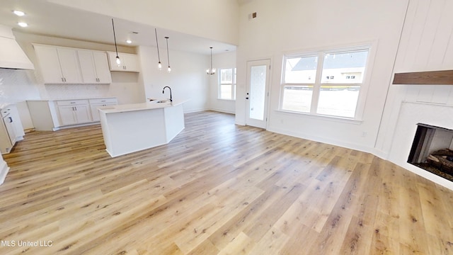 kitchen with white cabinets, hanging light fixtures, an island with sink, light wood-type flooring, and sink