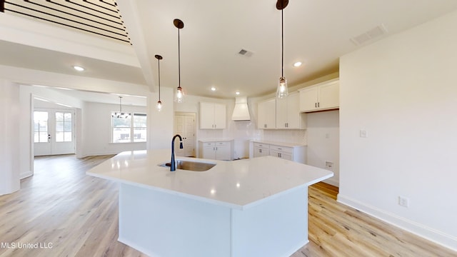 kitchen with hanging light fixtures, a large island with sink, white cabinetry, light wood-type flooring, and sink