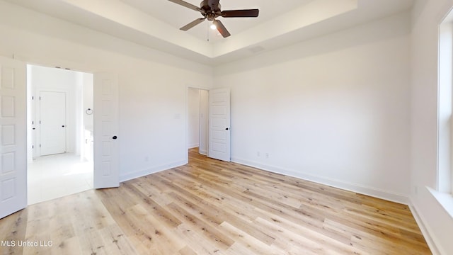 empty room with ceiling fan, light hardwood / wood-style floors, and a raised ceiling