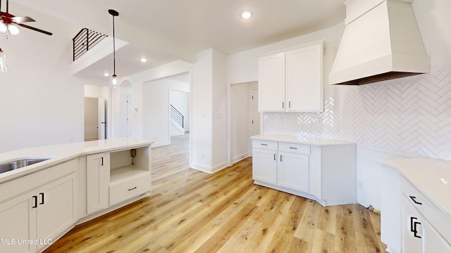 kitchen featuring white cabinets, custom range hood, pendant lighting, and light hardwood / wood-style floors