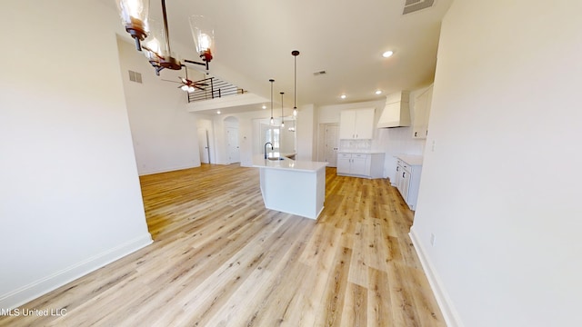 kitchen featuring custom exhaust hood, decorative backsplash, a center island with sink, white cabinetry, and light wood-type flooring