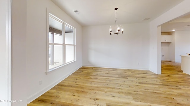 unfurnished dining area featuring an inviting chandelier and light hardwood / wood-style floors