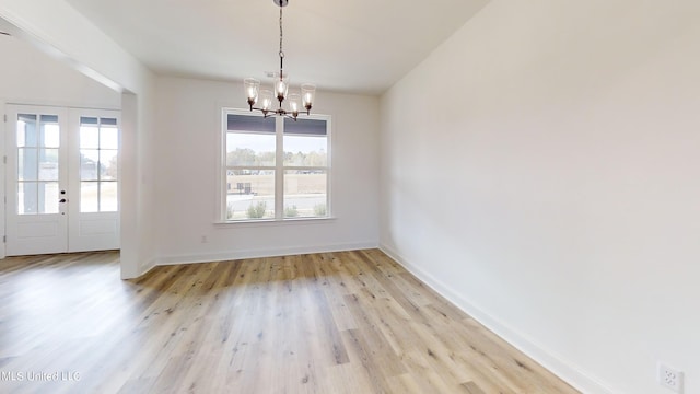 unfurnished dining area featuring an inviting chandelier, french doors, and light hardwood / wood-style floors