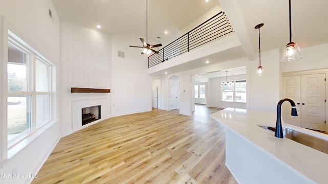 living room with sink, light hardwood / wood-style flooring, a high ceiling, and ceiling fan with notable chandelier