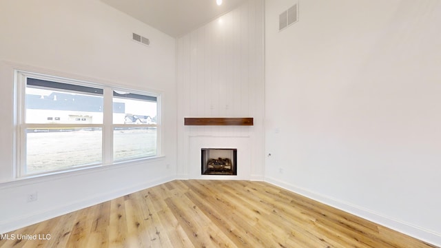 unfurnished living room with a large fireplace, high vaulted ceiling, light wood-type flooring, and wood walls