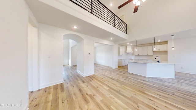 kitchen with a high ceiling, an island with sink, decorative light fixtures, light wood-type flooring, and white cabinets