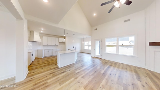 kitchen featuring a kitchen island with sink, pendant lighting, light wood-type flooring, white cabinetry, and premium range hood