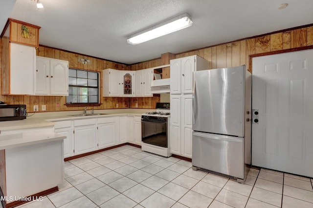kitchen featuring freestanding refrigerator, black microwave, gas range gas stove, wooden walls, and a sink