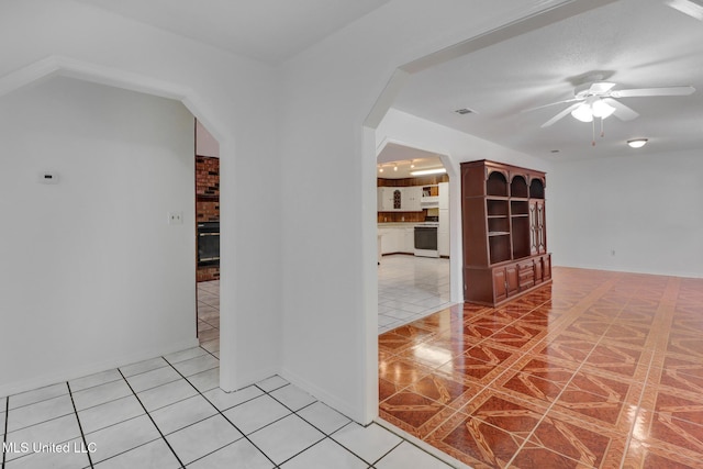 corridor featuring light tile patterned flooring, arched walkways, visible vents, and baseboards